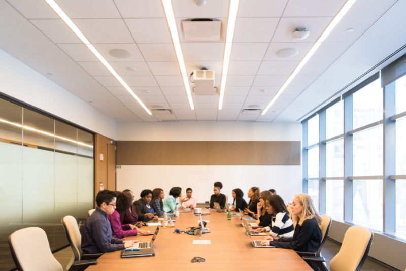 A meeting with 14 people sat around a board room table.