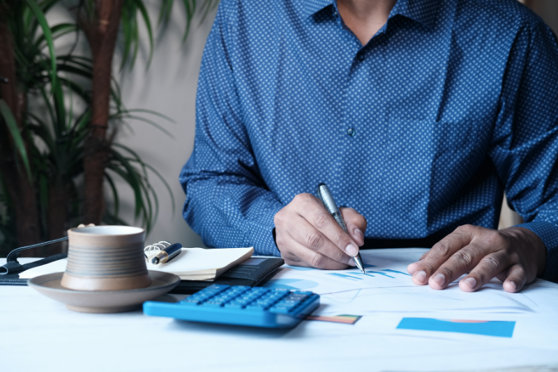 A man looking at some graphs at desk with a calculator and notepad