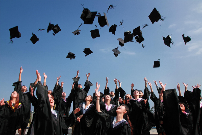 Graduates dressed in graduation gowns throwing their caps in the air.